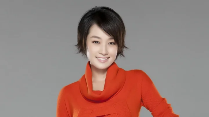 一名身穿红色毛衣的女性在灰色背景前微笑。