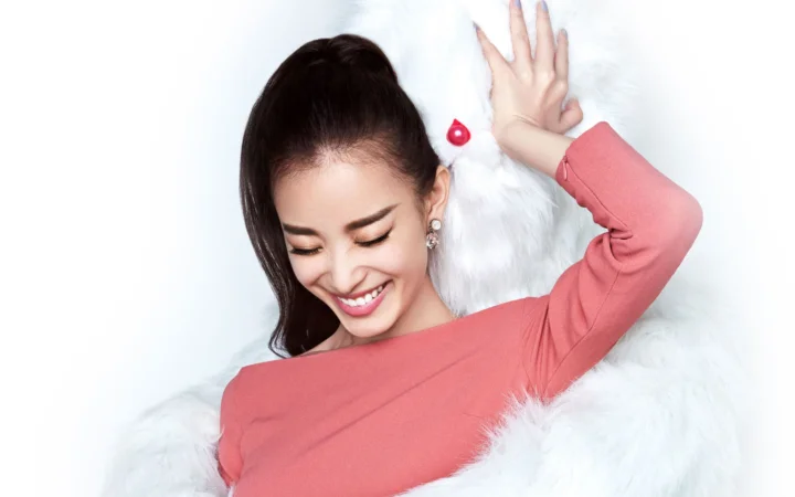 一名成年女性穿着粉色上衣躺在白色毛绒背景上微笑。