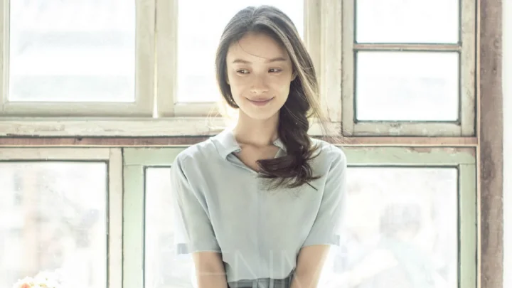 一名成年女性站在室内窗边，柔和光线映照着她的侧脸。