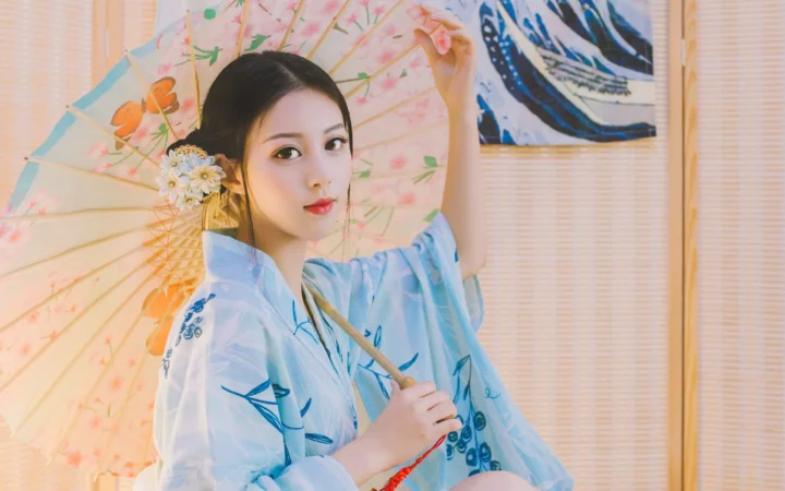 插画风格的成年女性身穿浅蓝色和服，手持花伞站在竹帘前。