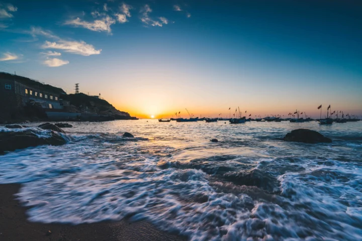 夕阳映照着海湾，海浪拍打着沙滩，远处停泊着几艘小船。