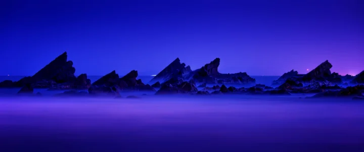 蓝紫色天空映照着远处嶙峋的山峰，前景被朦胧雾气覆盖。
