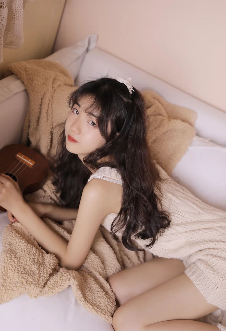 一名长发女子坐在床上，手边放着一把吉他。