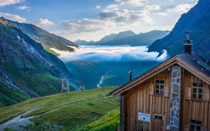 群山環繞的山谷中雲海翻湧，前景是一座木屋。