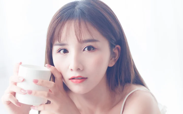 一名女子手捧白色杯子面对镜头，画面明亮柔和。