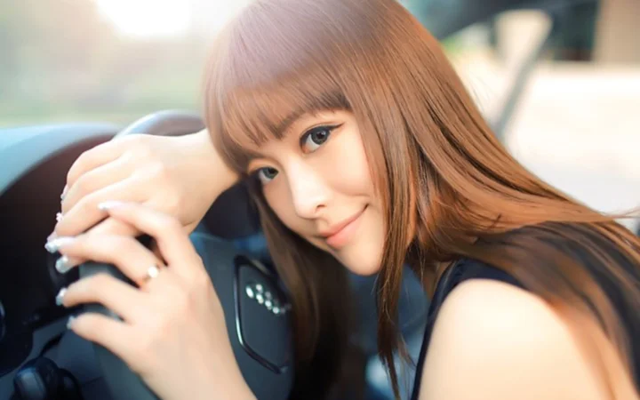 一名棕色长发女性靠在车内座椅旁微笑看向镜头。