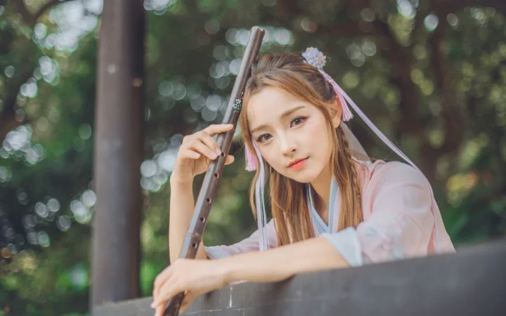 一位身穿传统服饰的成年女子在树林中手持笛子。