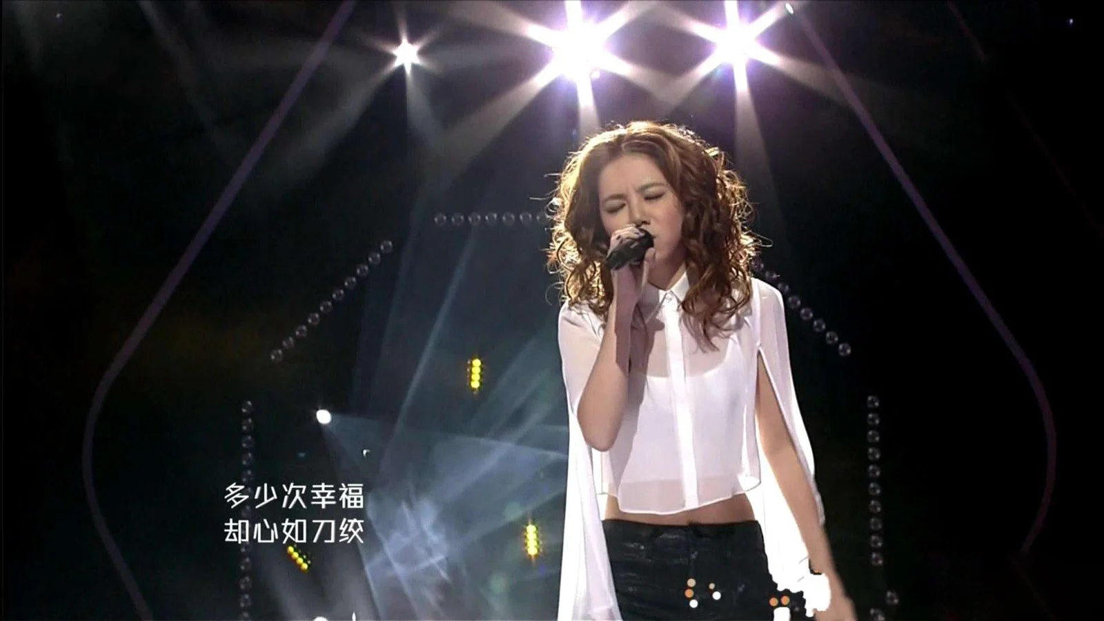 一位成年女歌手手持麦克风在聚光灯下进行舞台演唱。