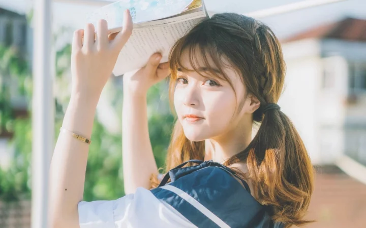一名女子在明亮的窗边举着一本书，阳光映照着她的侧脸。