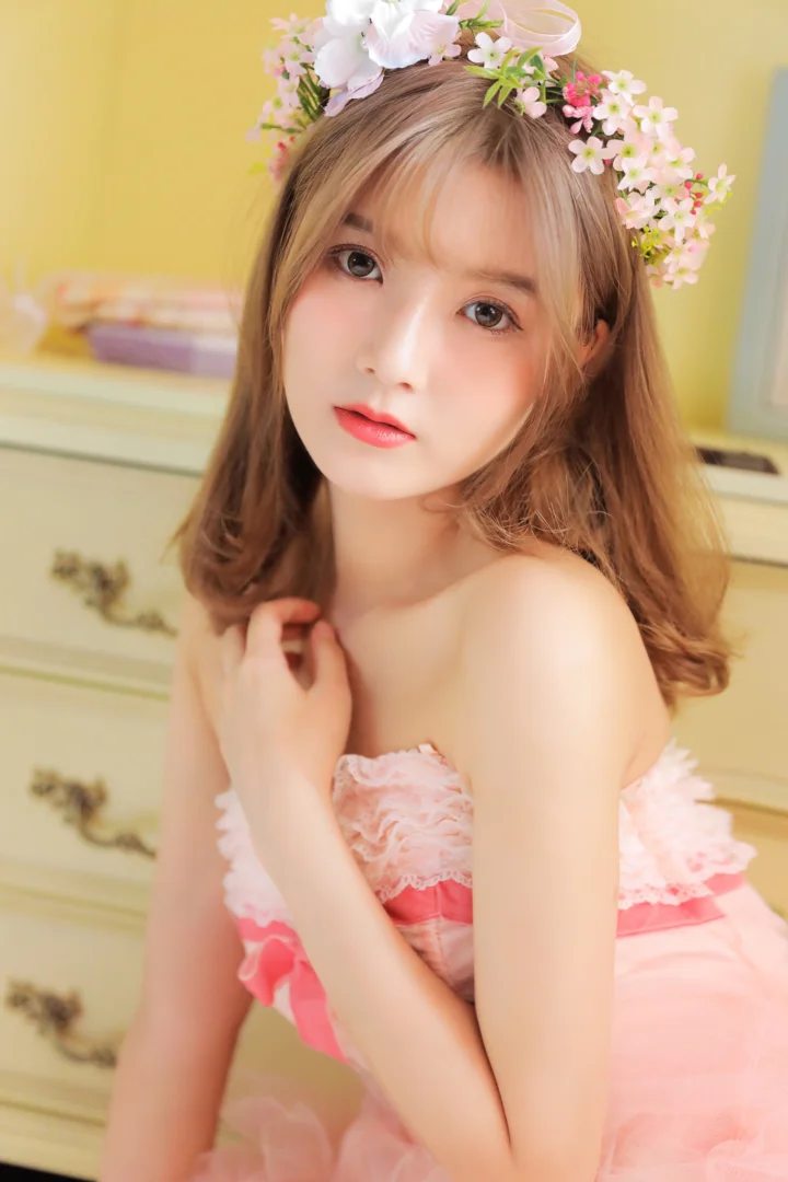 花冠を身につけ、ピンクのドレスを着た女性が室内でカメラを見つめている。