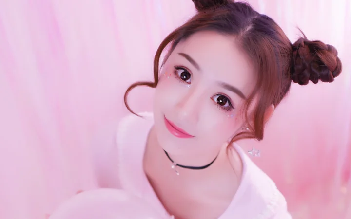 一名盘发女性以近距离肖像姿态面对镜头，背景和画面整体呈粉色调。