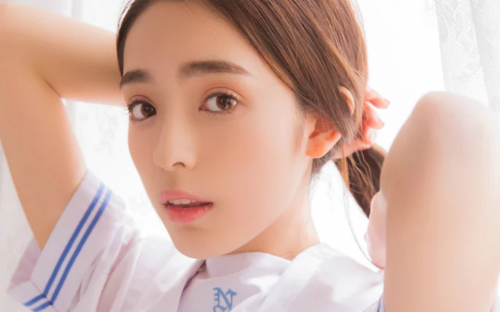 一名棕色头发的成年女性身穿白色上衣，在柔和光线下以近距离人像姿势面对镜头。