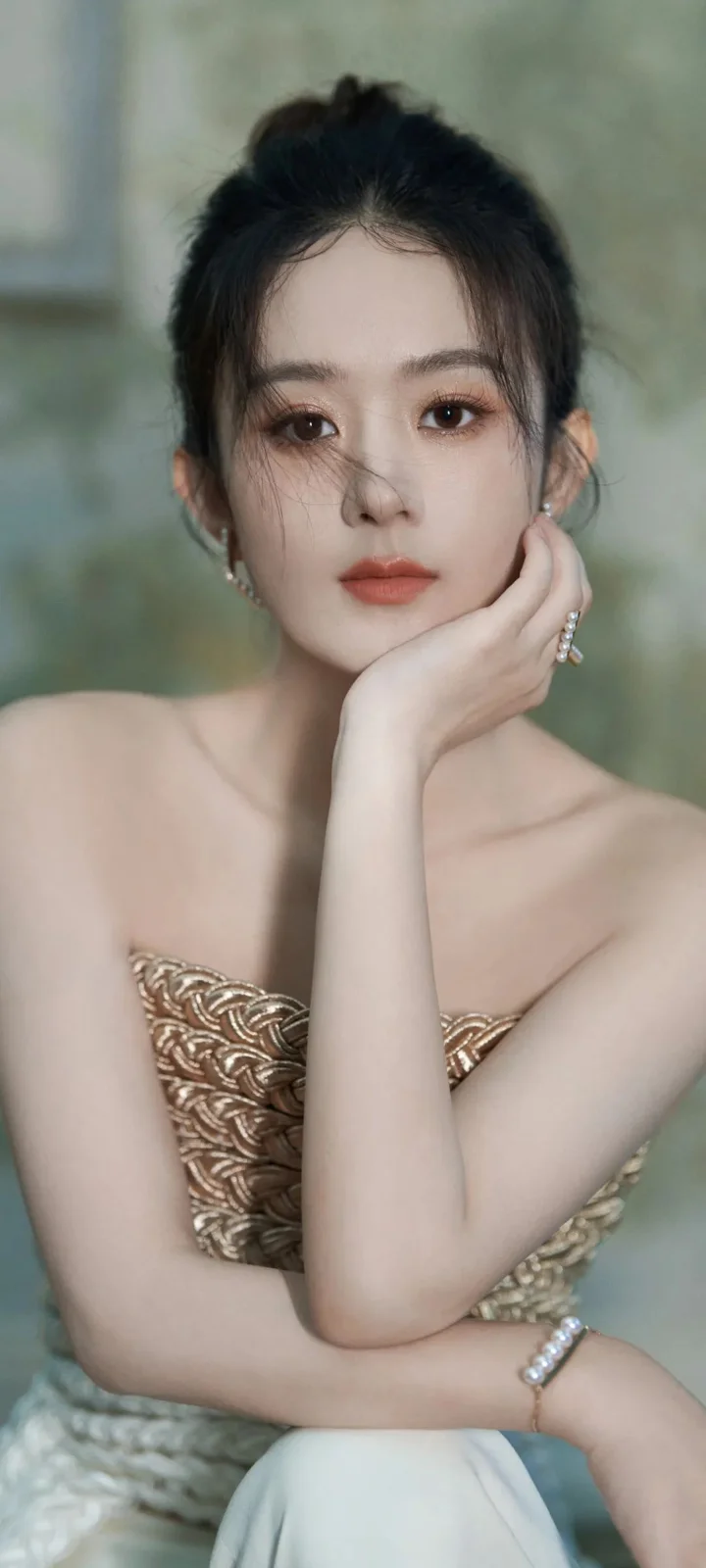 一位成年女性身穿金色礼服，托腮注视镜头。