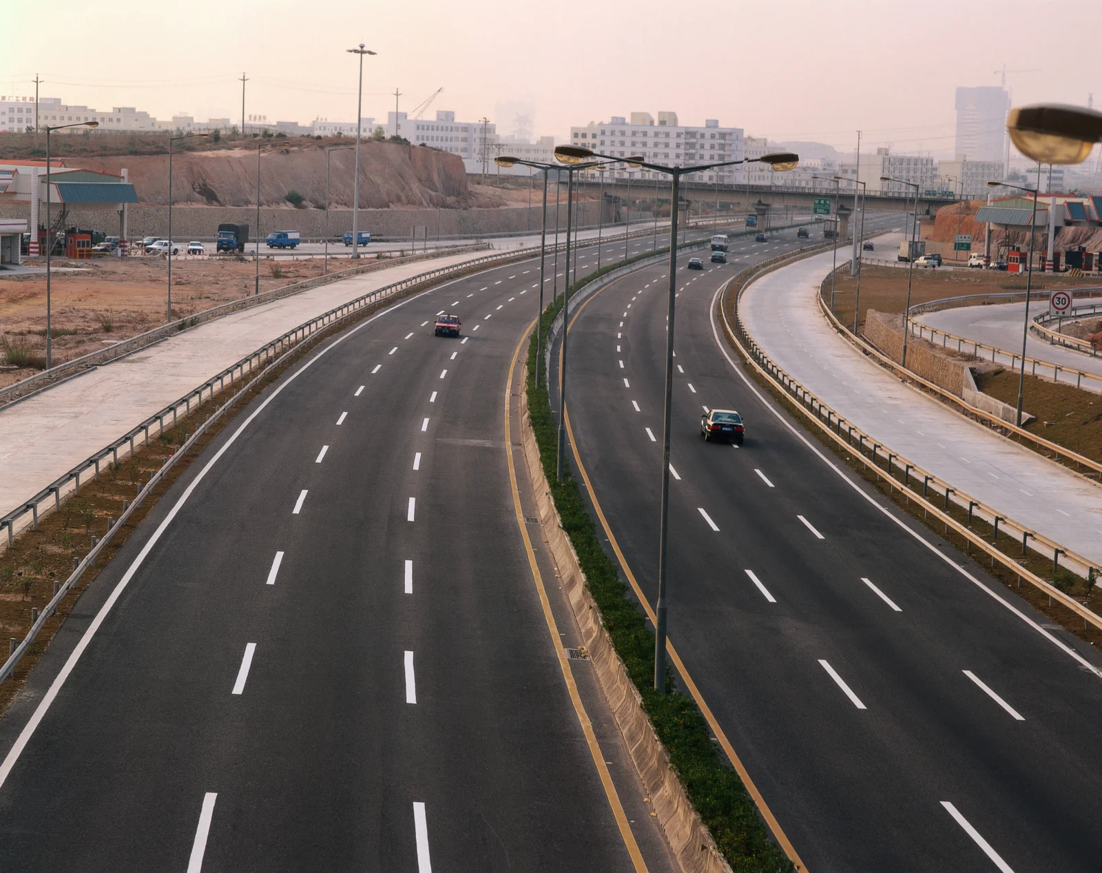 宽阔的城市高速公路穿过建筑群，路旁排列着高大的路灯。