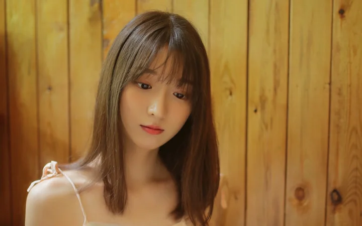 나무 벽 앞에 여성이 서 있는 따뜻하고 자연스러운 인물 사진입니다.