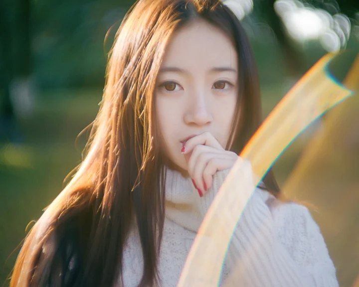 一名长发女子穿着白色针织衫，在户外柔和阳光下望向镜头。