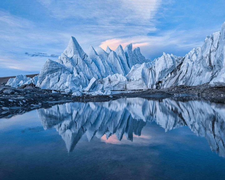 冰川覆盖的尖峭雪山倒映在宁静的蓝色湖水中。