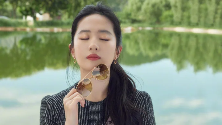 一名闭着眼睛的女子在湖边手持太阳镜。