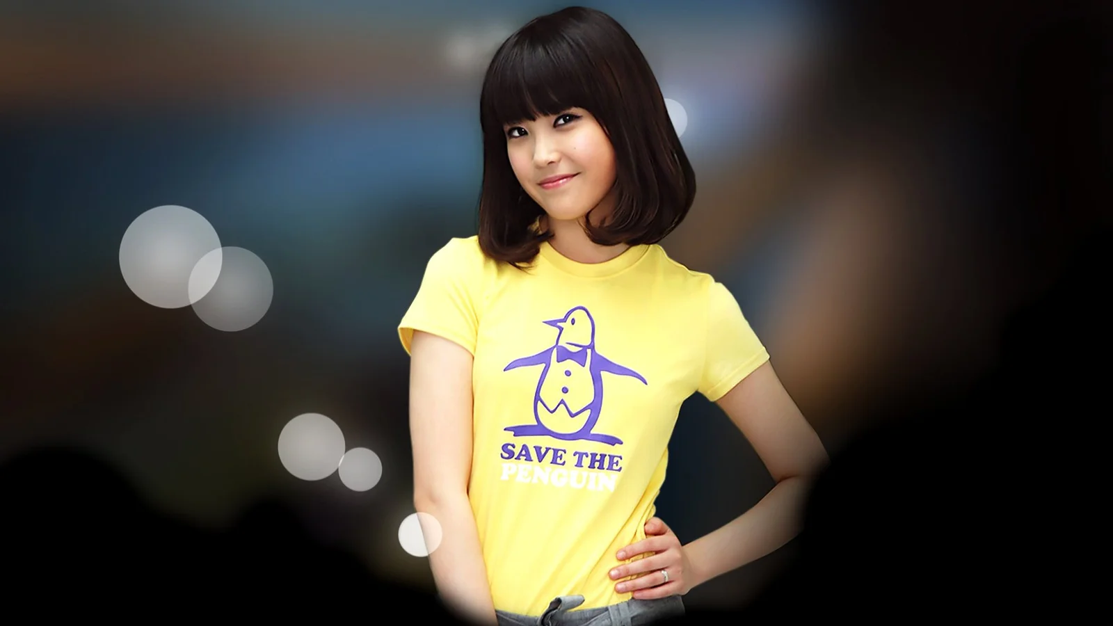 黄色いTシャツを着た成人女性が、ぼかした暗い背景の前に立っています。