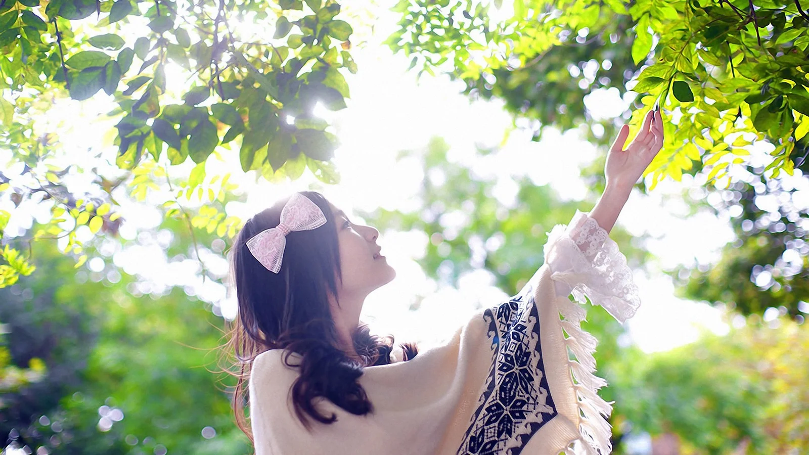 木漏れ日の下で女性が枝葉に手を伸ばしている。