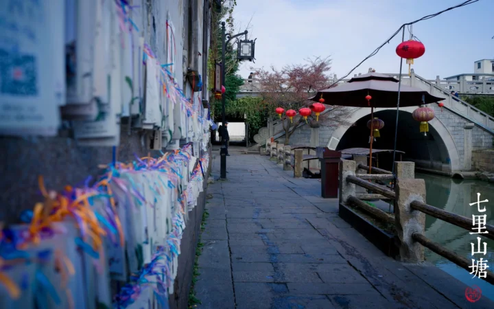 石板步道沿着 canal 通向一座装饰着红灯笼的古老石桥。