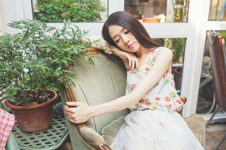 一名身穿花卉连衣裙的女子坐在扶手椅上，身旁摆放着盆栽植物。