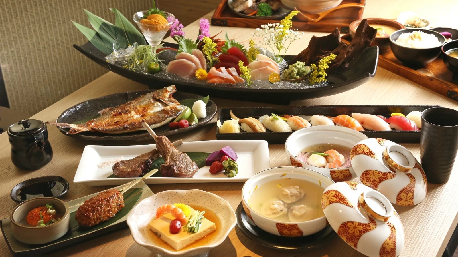 寿司、焼き魚、汁物、茶器などのさまざまな和食が食卓に並んでいます。