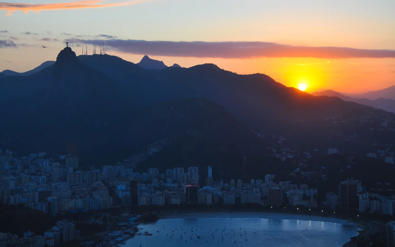 夕阳映照山脉剪影，密集城市建筑与海湾铺展在下方。