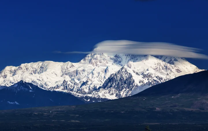 壮丽的雪山被白云环绕，前景是深色山坡与山谷。