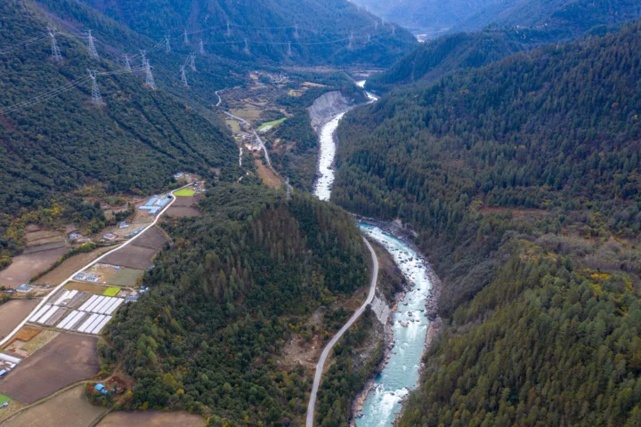 群山与森林环绕的山谷中，一条白色河流蜿蜒穿过农田和道路。