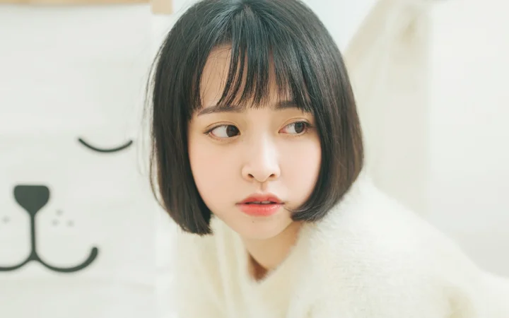 一名留着齐耳短发的女生穿着浅色毛衣，侧头望向画面右侧。