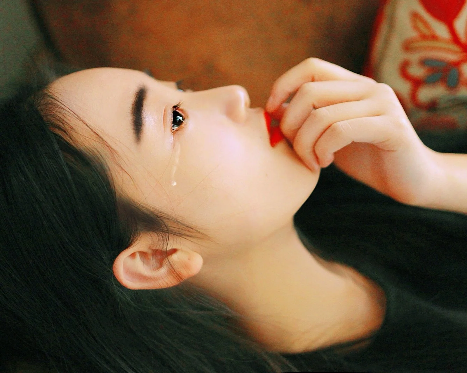 一名黑发女子侧躺着，手指靠近嘴唇，脸颊上有一滴泪水。
