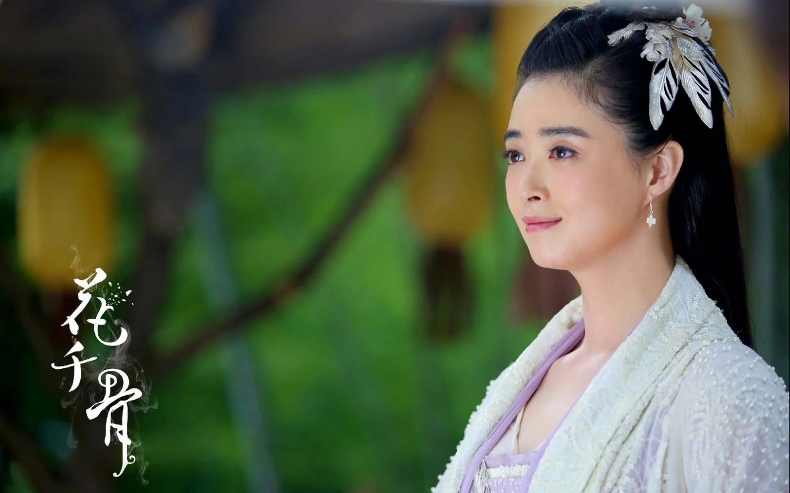 一位佩戴发饰、身穿传统服饰的成年女性站在绿色虚化背景前。