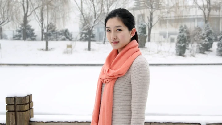 一名成年女子站在积雪覆盖的户外环境中，佩戴珊瑚色围巾。