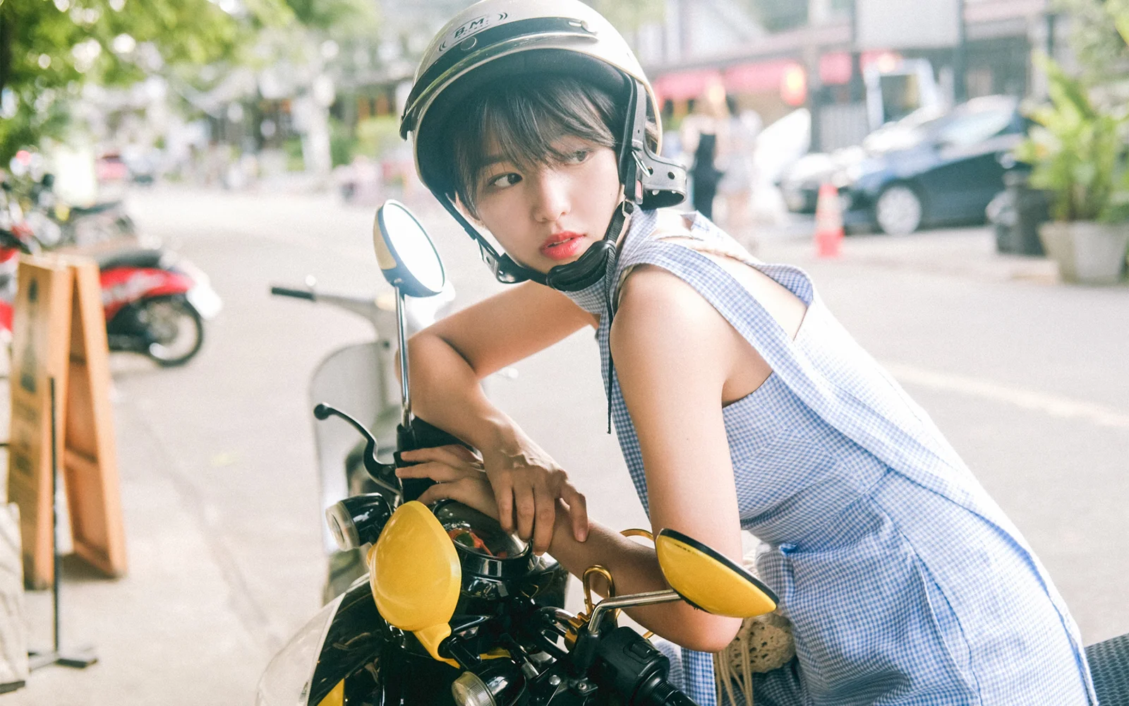一名戴着头盔的女子坐在街边的摩托车上回头看向镜头。