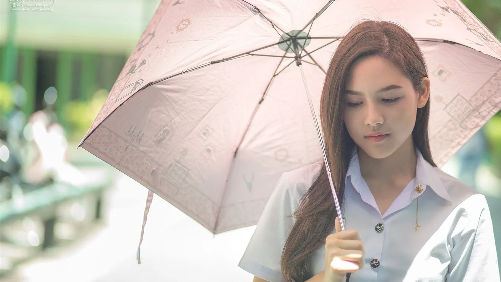 一名年轻女子在户外撑着一把浅粉色雨伞。