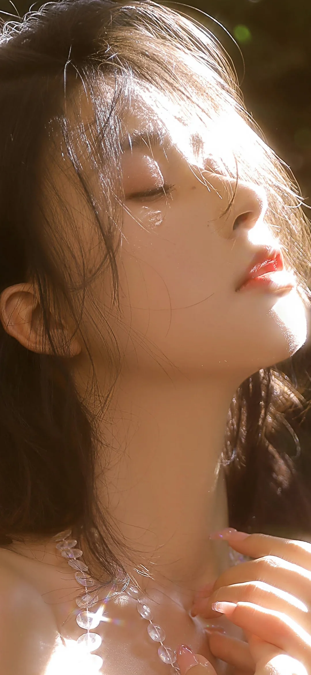 一位女性在温暖阳光下闭眼侧脸，手指轻触透明项链。
