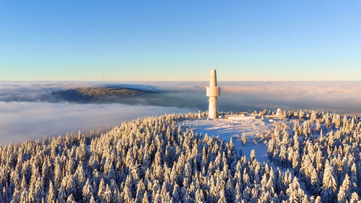 积雪覆盖的森林延伸至山脊，一座高塔矗立在云海之上。