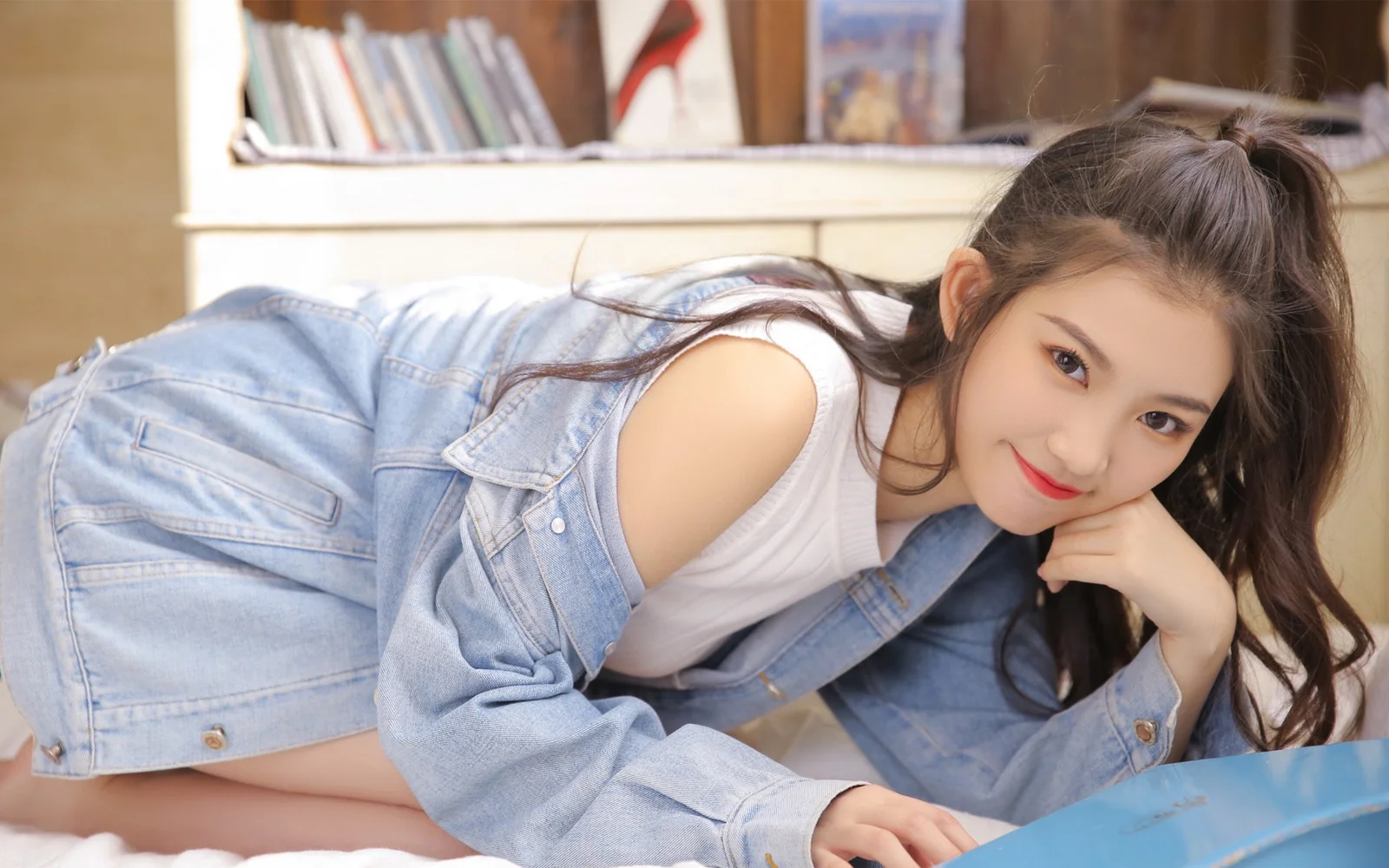 데님 의상을 입은 성인 여성이 실내에서 카메라 가까이 포즈를 취하고 있습니다.