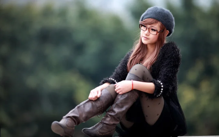 一名戴着贝雷帽和眼镜的成年女性坐在户外树木背景前。