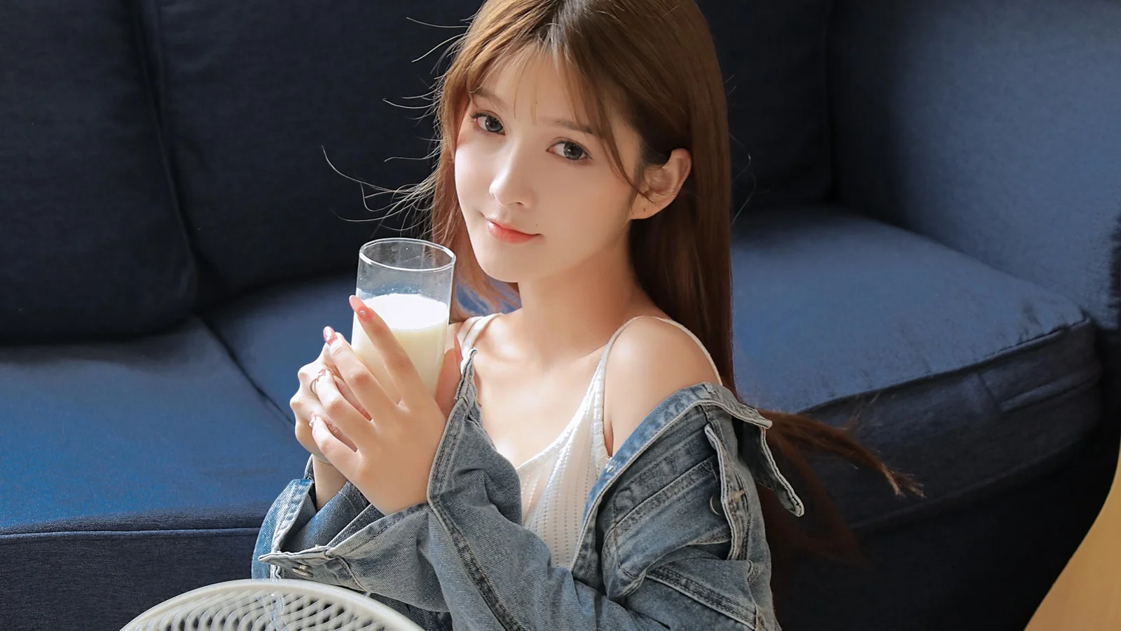 一名成年女性坐在深色沙發上，手持一杯飲品。