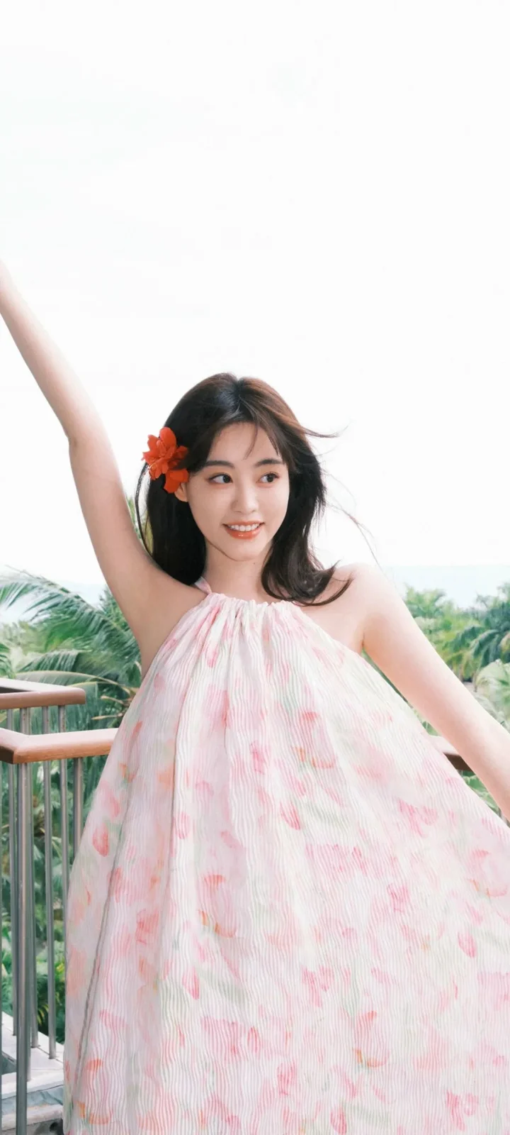 一名女子穿着粉色连衣裙站在阳台上，背景可见热带植物。