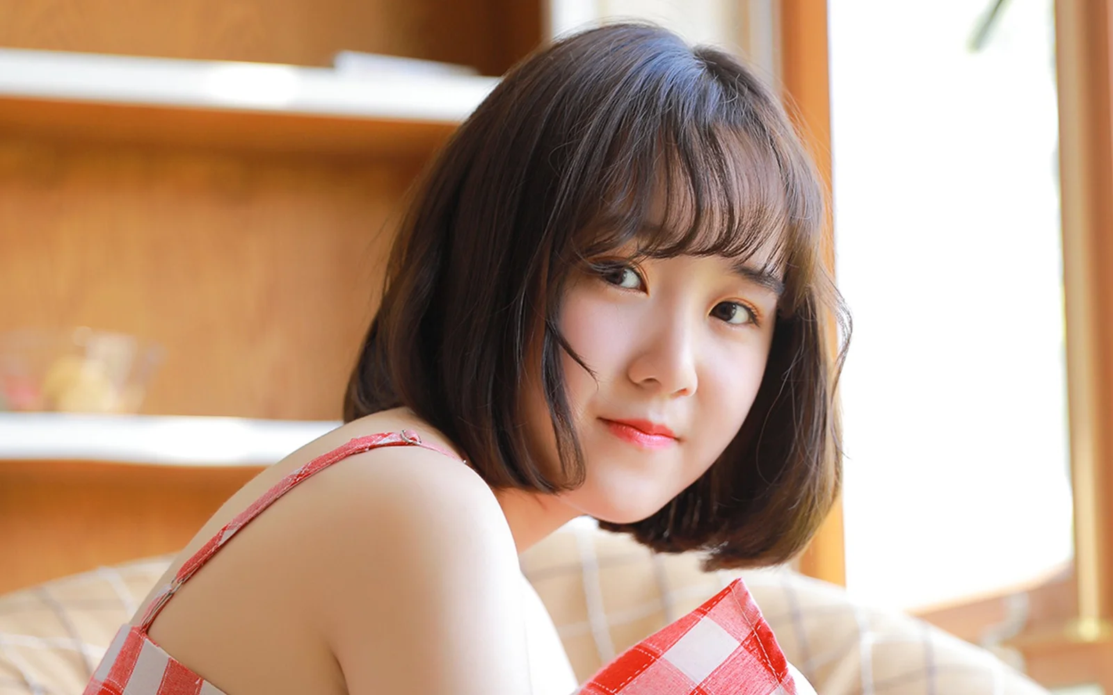 一位短髮女性坐在室內窗邊，面向鏡頭微笑。