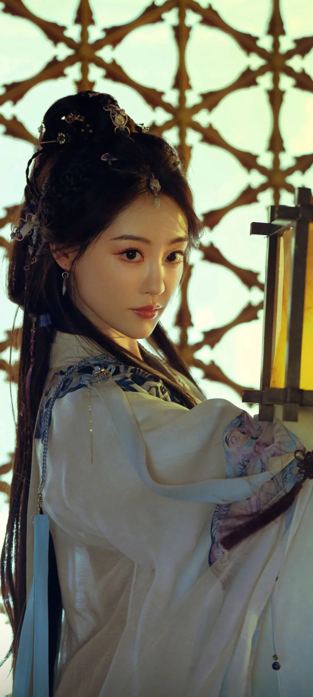 전통 의상을 입은 여성이 장식 격자창 앞에서 등불을 들고 있다.