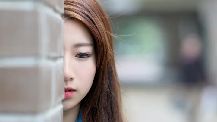 一名棕色长发女性隔着玻璃露出半张脸，背景柔和虚化。