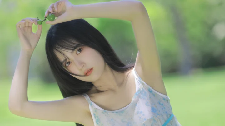 一名黑发女子在绿色户外背景前举起双臂，手中拿着一小枝绿叶。