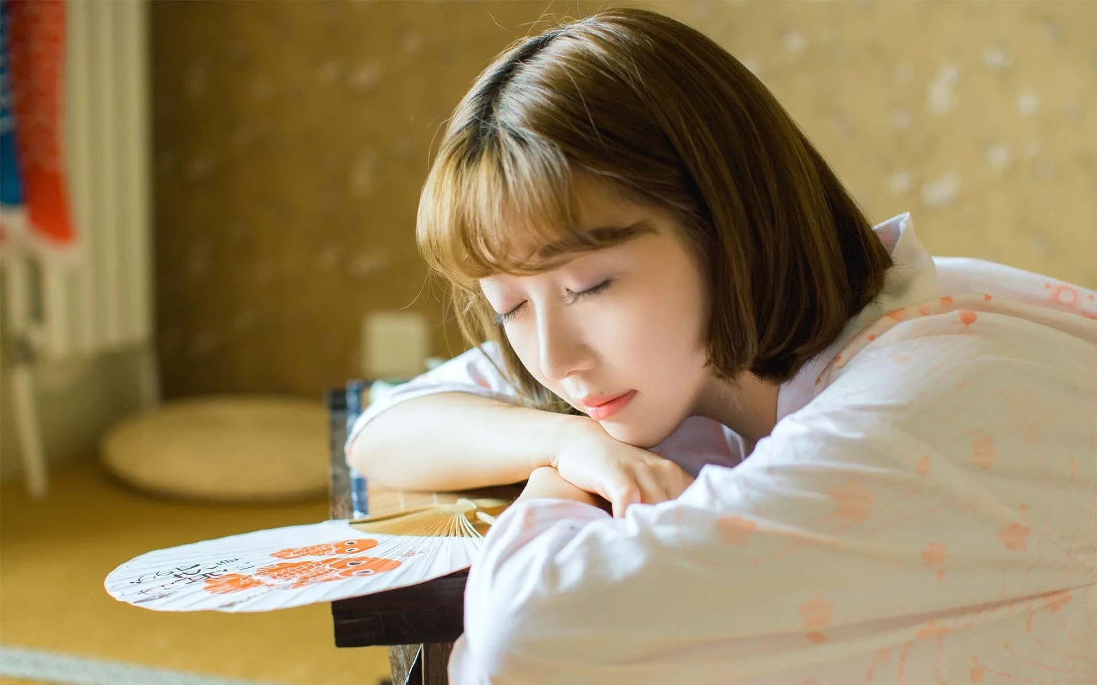 따뜻한 실내에서 젊은 여성이 눈을 감고 테이블에 기대어 쉬고 있습니다.