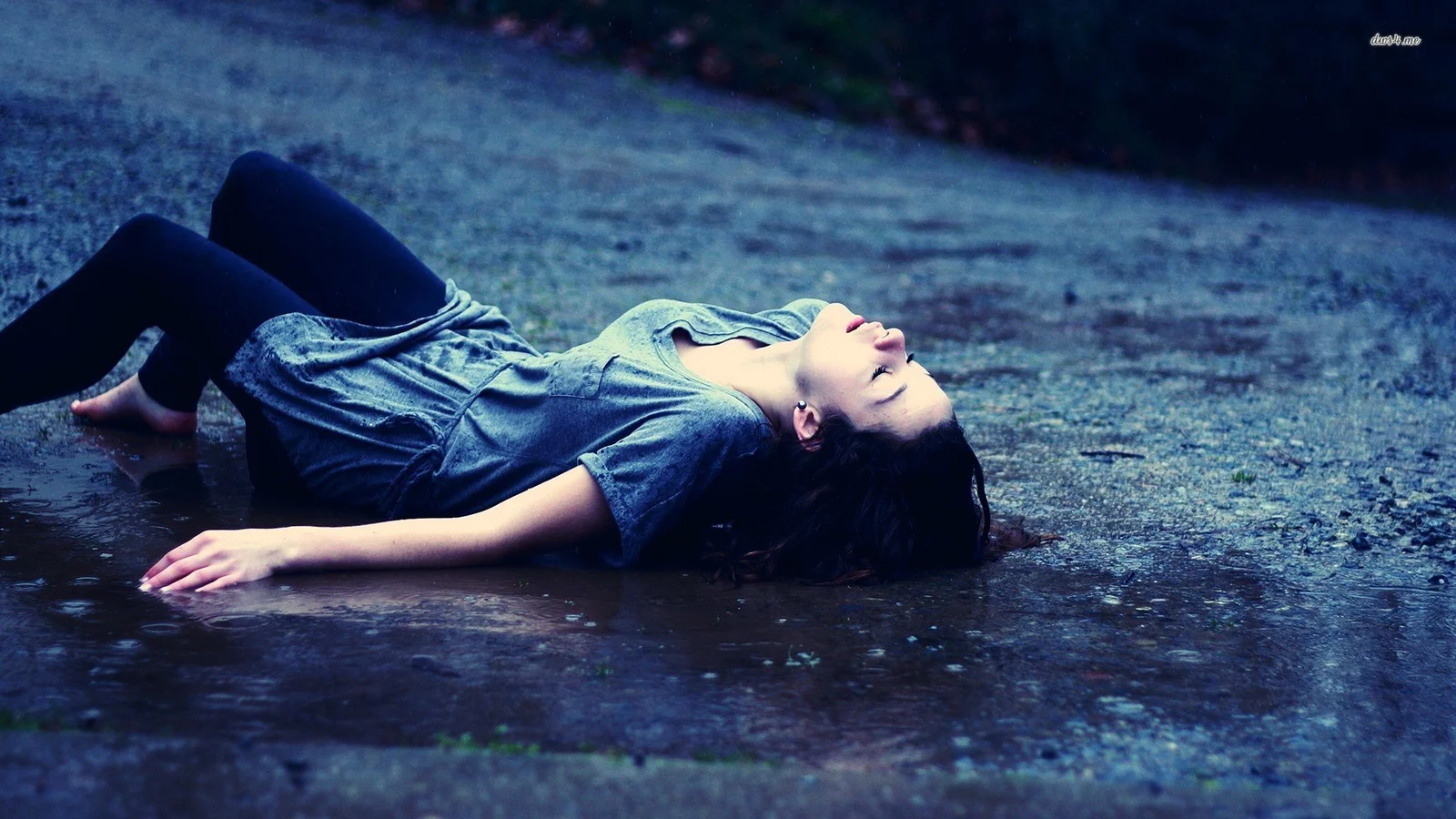 一名穿着深色衣服的成年女性躺在雨水形成的浅水洼中。