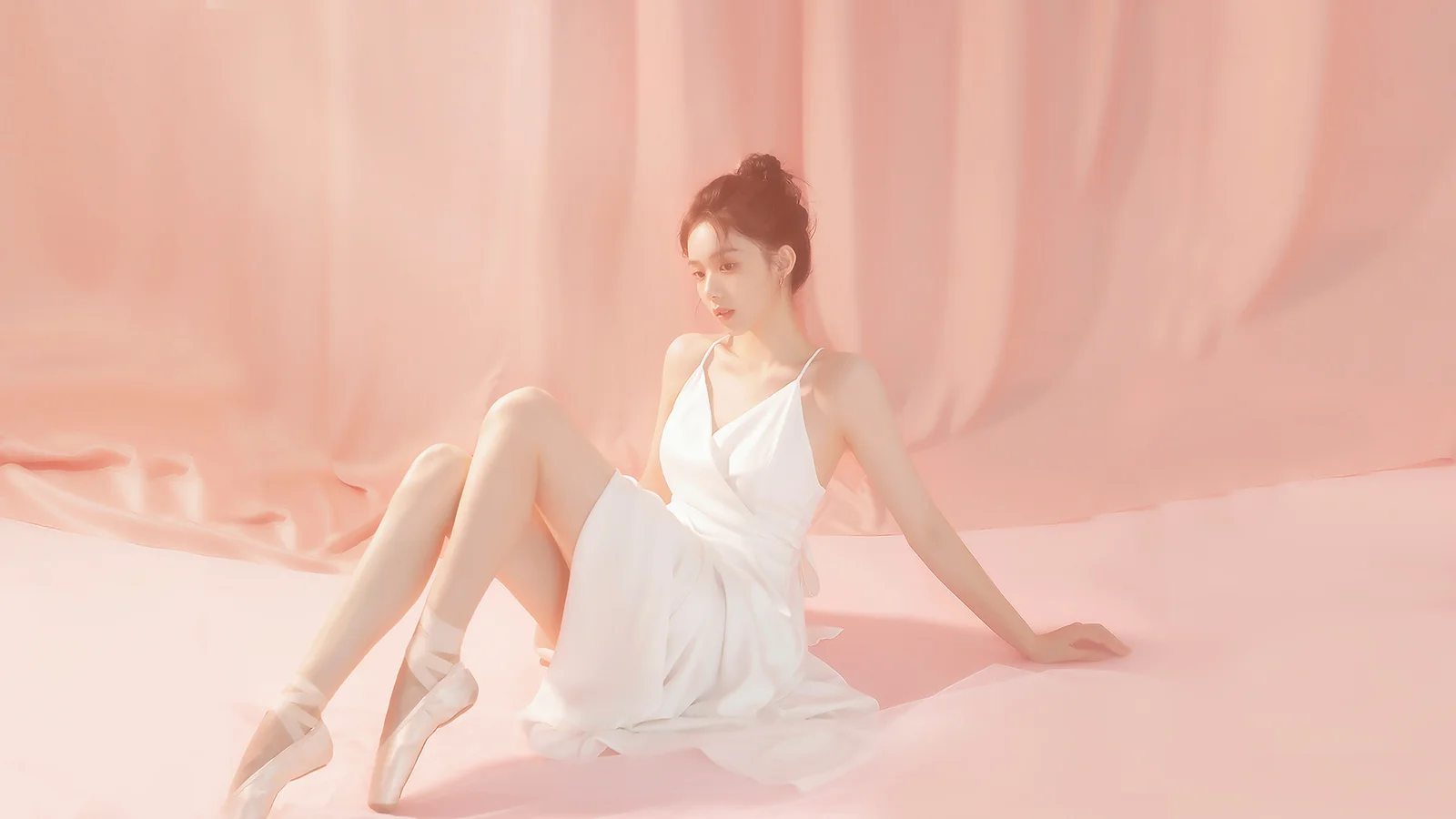 흰색 드레스를 입은 성인 여성이 분홍색 배경 앞에 앉아 있습니다.