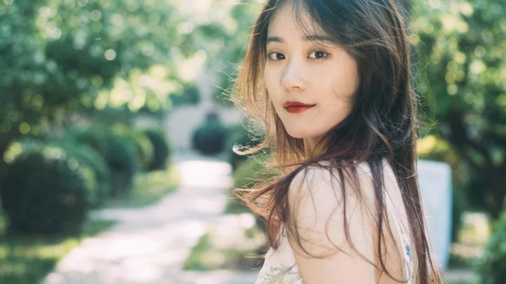 一名成年女性站在阳光洒落的花园小径旁回望镜头。